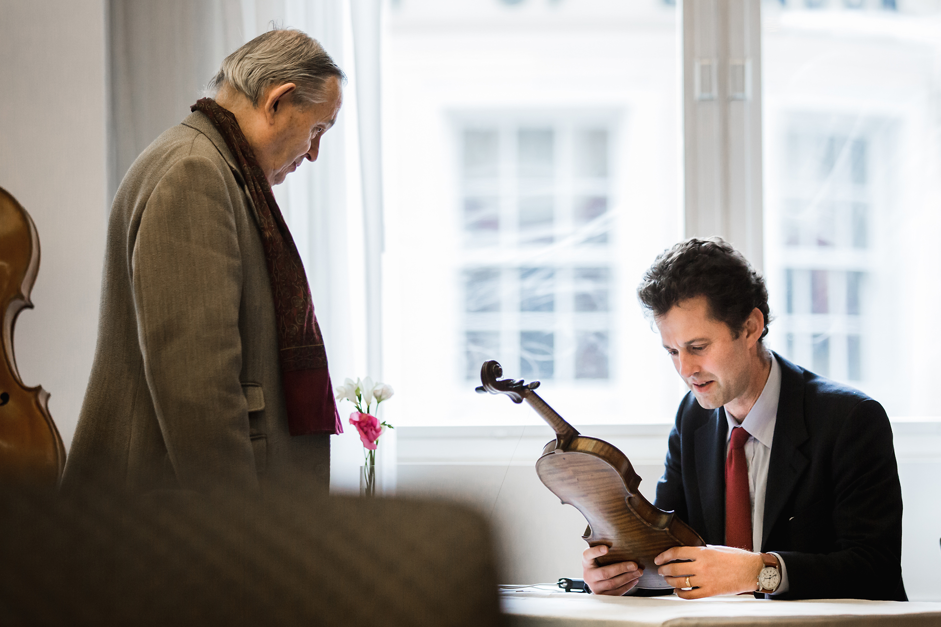 An Amati specialist examining a violin at the window while its owner looks on, at a London viewing.